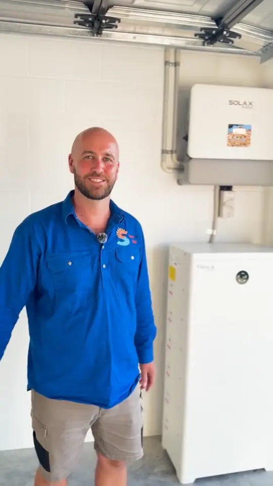 Gus in a Sunnyville Solar shirt beside a SolaX inverter and battery